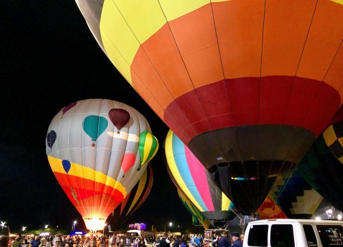 Colorful hot air balloons illuminated at night, surrounded by a crowd of people enjoying the event.