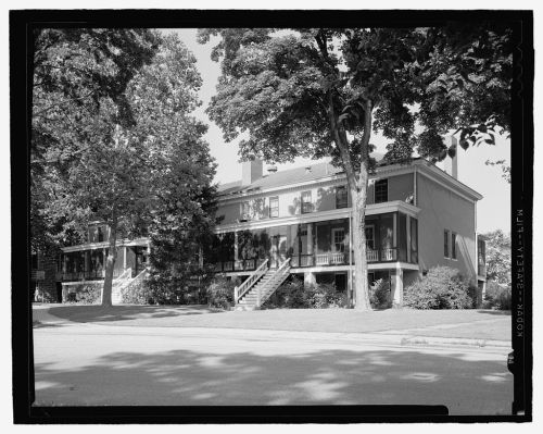 Historic building with a porch, surrounded by trees, captured in black and white.