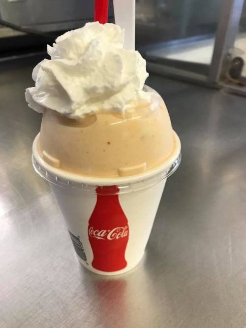 A cup of creamy dessert topped with whipped cream and a red straw, featuring a Coca-Cola logo on the cup.