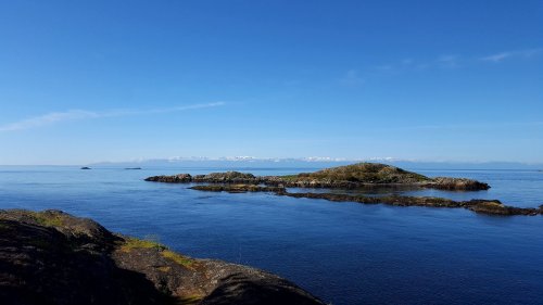 A serene coastal scene featuring calm blue waters, rocky islands, and a clear sky with distant mountains.