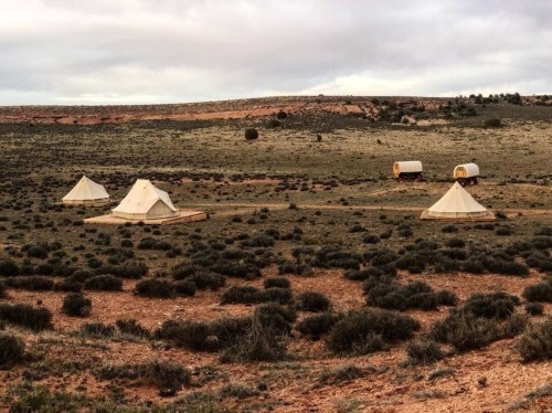 A serene landscape featuring several tents and trailers set against a grassy, rocky terrain under a cloudy sky.