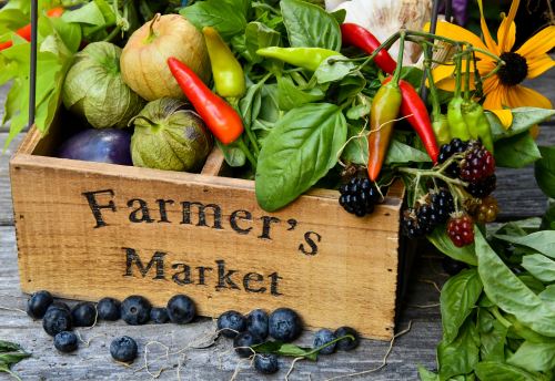 A wooden crate labeled "Farmer's Market" filled with fresh vegetables, herbs, and berries on a rustic wooden surface.