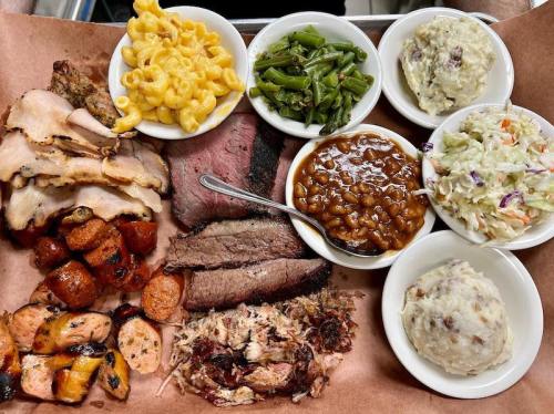 A platter of barbecue meats including brisket, sausage, and pulled pork, served with sides of mac and cheese, green beans, and coleslaw.