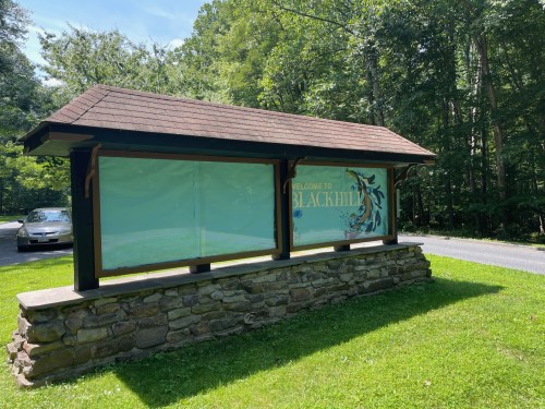 A welcome sign for Blackhill, set in a green area with trees, featuring a stone base and a covered display area.