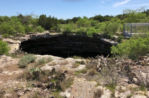A large sinkhole surrounded by rocky terrain and greenery, with a viewing platform nearby.