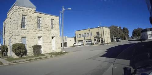 A sunny street view featuring a stone building and a two-story commercial building in a small town.