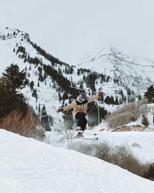 A skier performs a jump on a snowy slope with mountains in the background.