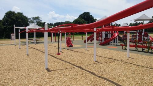 A playground featuring red slides, swings, and a sandy area under a clear blue sky.