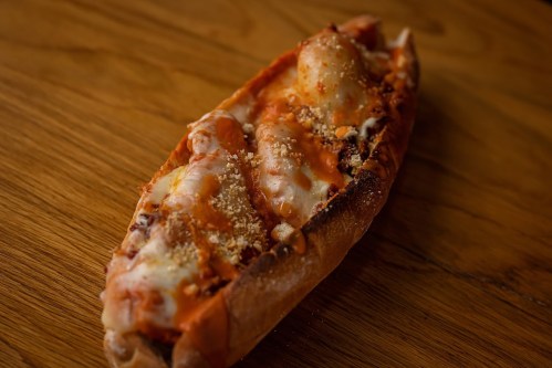 A cheesy, baked potato topped with sauce and breadcrumbs, resting on a wooden surface.
