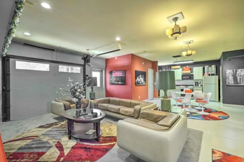 Modern living room with a stylish sofa, colorful rug, and open kitchen area, featuring vintage Coca-Cola art on the walls.