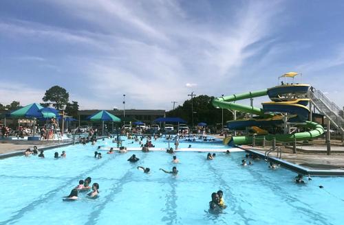 A busy outdoor pool with children swimming and a large water slide in the background under a blue sky.
