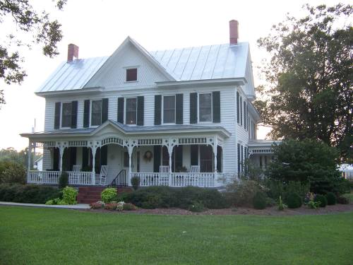 A large white Victorian-style house with green shutters, a porch, and a well-maintained lawn.