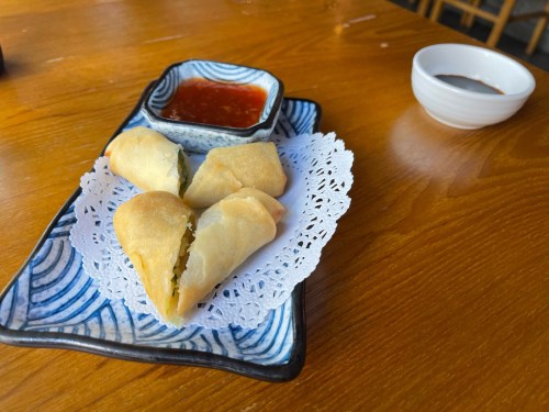 A plate of spring rolls with a side of dipping sauce, resting on a wooden table.