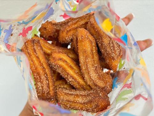 A hand holding a colorful bag filled with freshly made, golden-brown churros coated in sugar.