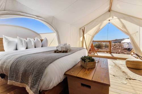 Cozy glamping tent interior with a large bed, wooden furniture, and a view of the outdoors through an open entrance.