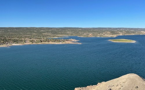 A scenic view of a calm lake surrounded by green hills and clear blue skies.