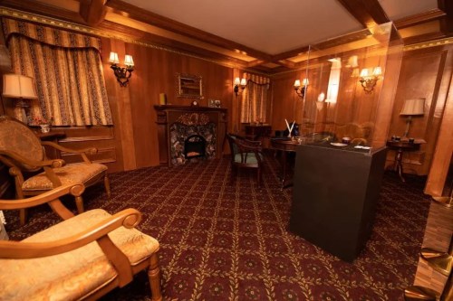 Cozy room with wooden walls, patterned carpet, vintage furniture, and a fireplace, creating a warm, inviting atmosphere.