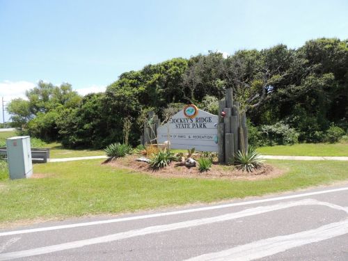 Sign for Dokens Ridge State Park, surrounded by greenery and plants, with a clear blue sky above.