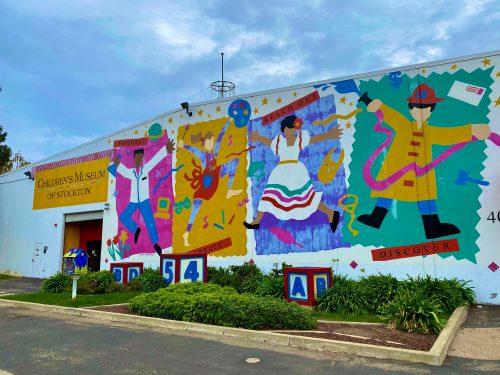 Colorful mural on the side of the Children's Museum of Stockton, featuring playful characters and vibrant designs.