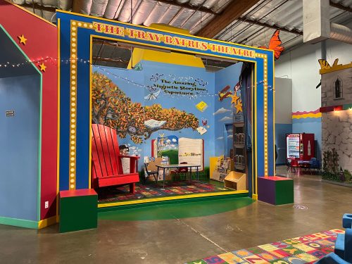 A colorful children's theater stage with a large red chair, storybook decorations, and a whimsical backdrop.