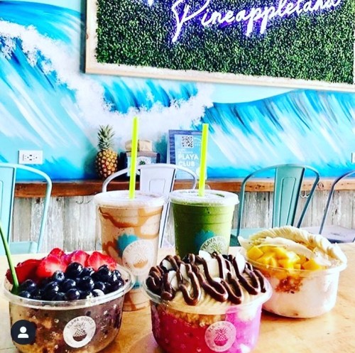 Colorful smoothies and acai bowls with fresh fruit, set against a vibrant wave-themed backdrop.