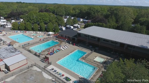 Aerial view of Strawberry Park featuring multiple swimming pools, a building, and surrounding greenery.
