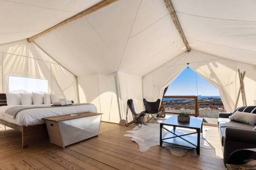 Cozy glamping tent interior with a bed, seating area, and a view of the outdoors through an open entrance.