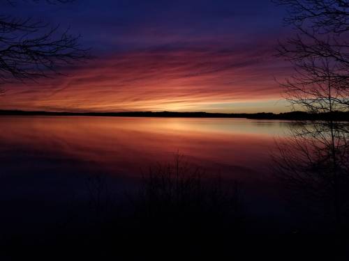 A serene sunset over a calm lake, with vibrant purple and orange hues reflecting on the water's surface.