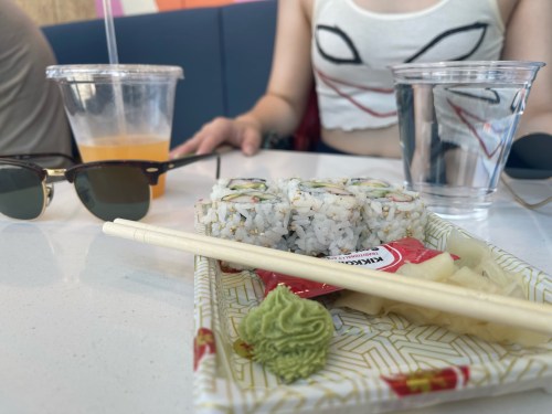 A table with sushi, wasabi, pickled ginger, drinks, and sunglasses in a casual dining setting.