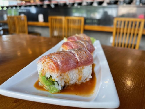 A close-up of sushi rolls on a white plate, featuring rice, lettuce, and slices of fish, drizzled with sauce.