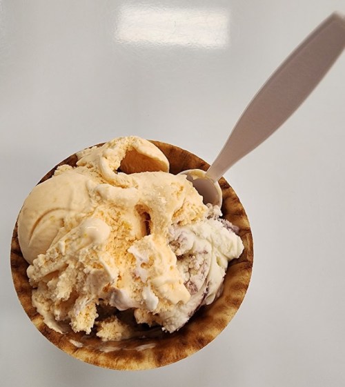 A bowl of ice cream with various flavors, including orange and white, topped with a plastic spoon.