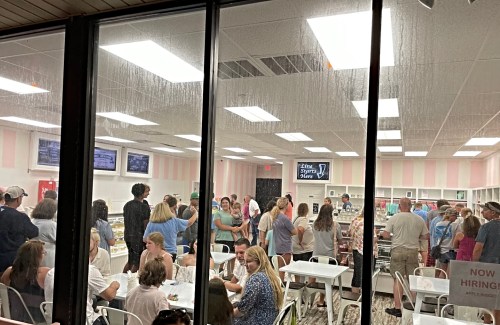 A busy ice cream shop filled with customers, some seated and others in line, with a bright, cheerful interior.