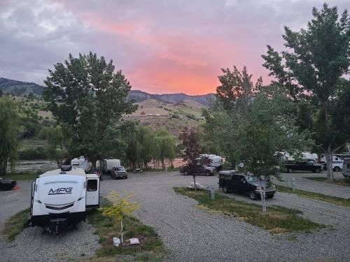 A scenic campsite with RVs and trees, set against a colorful sunset over rolling hills.