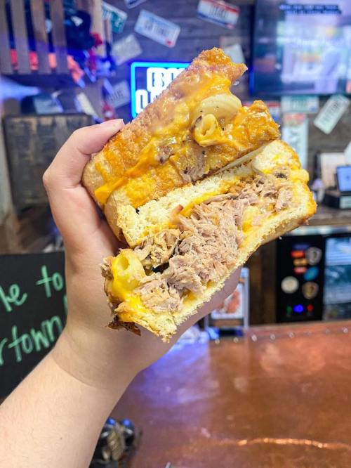A hand holding a thick sandwich filled with pulled pork and melted cheese, with a crispy bread exterior.