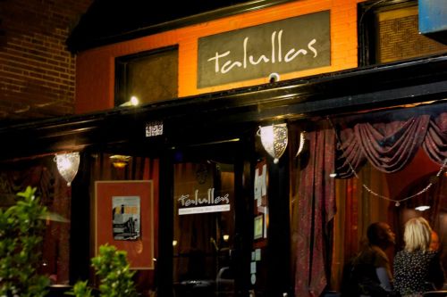 Exterior of Talullas restaurant at night, featuring a warm glow and decorative curtains.