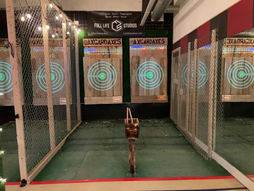 Axe throwing venue with multiple targets featuring blue bullseyes, surrounded by a protective fence.