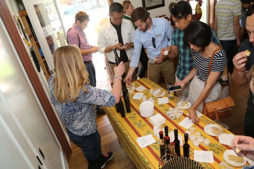 A group of people sampling oils and foods at a tasting event, gathered around a table with various products.
