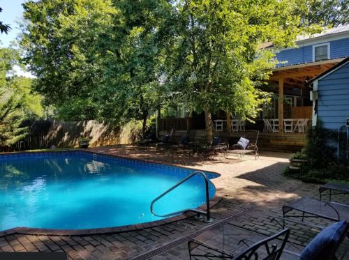 A sunny backyard with a blue pool, surrounded by trees and a wooden deck with seating.