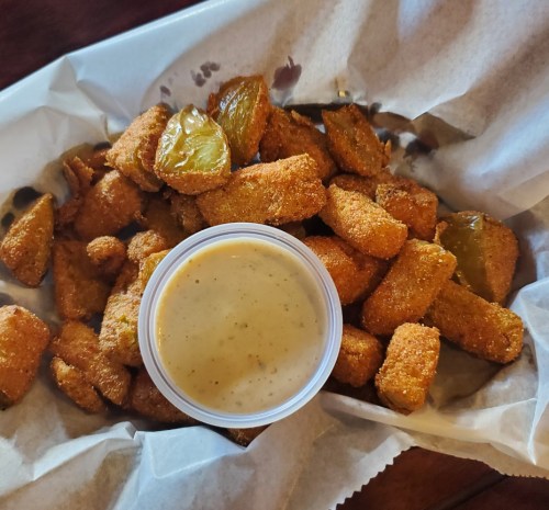 A basket of golden-brown fried pickles served with a creamy dipping sauce.