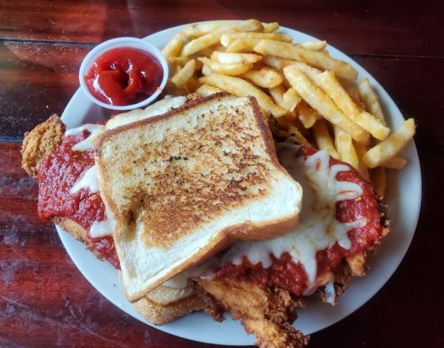 A plate of crispy fried chicken topped with marinara sauce and melted cheese, served with fries and a side of ketchup.
