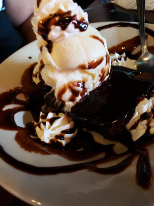 A decadent dessert featuring a chocolate brownie topped with vanilla ice cream, whipped cream, and chocolate sauce.