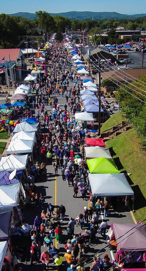 Aerial view of a bustling street fair with numerous tents and a large crowd of people enjoying the event.