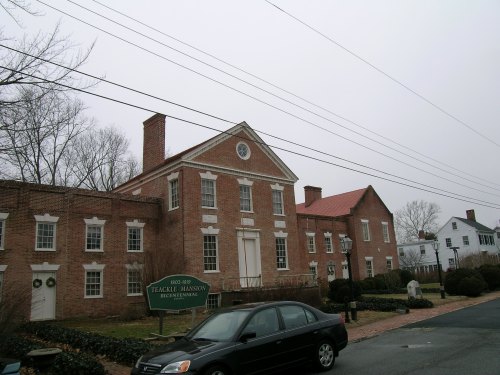 Historic Teackle Mansion in Buckhannon, featuring red brick architecture and a cloudy sky. Car parked in front.