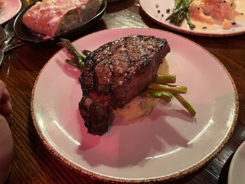 A grilled steak on a bed of mashed potatoes, garnished with asparagus, served on a white plate.