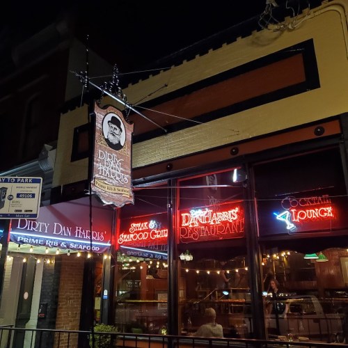 A nighttime view of Dirty Dan Harris's restaurant, featuring illuminated signs for dining and a cozy atmosphere.