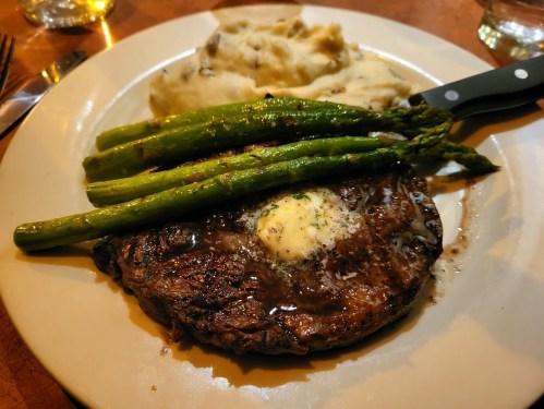 A plate featuring a grilled steak topped with butter, served with mashed potatoes and asparagus.