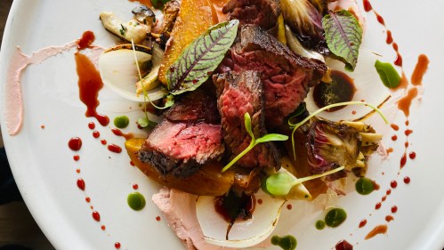 A beautifully plated dish featuring sliced beef, colorful vegetables, and garnishes on a white plate with sauces.
