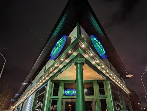 A corner view of a restaurant with illuminated signs reading "Melrose Grill" and "OPEN" at night.