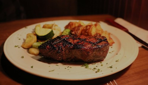 A beautifully grilled steak served with roasted potatoes and sautéed vegetables on a white plate.