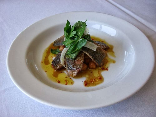 A plated dish featuring fish fillets topped with herbs and served with beans in a flavorful sauce.